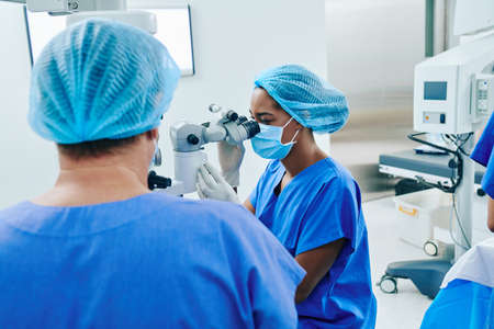 Young female Black surgeon getting ready for laser vision correction with usage of modern equipmentの写真素材