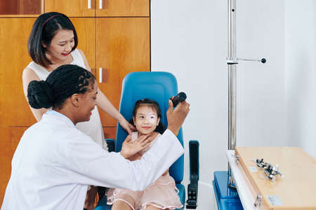 Pediatric ophthalmologist using flashlight when checking eyesight of little smiling girlの写真素材