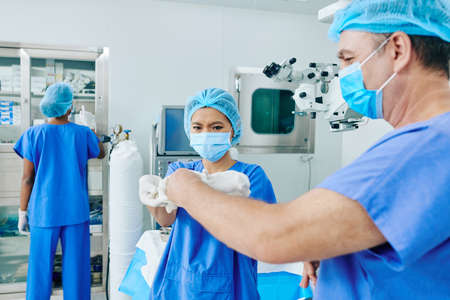 Young assistant helping surgeon to put on sterilized surgical gloves in operating roomの写真素材