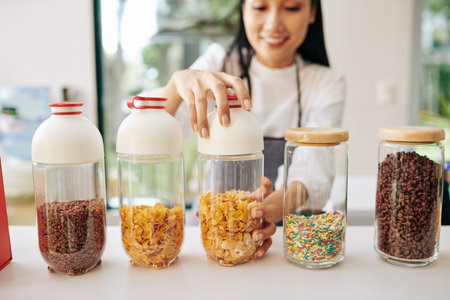 Smiling Vietnamese waiter opening container with corn flakes to make breakfast for customer