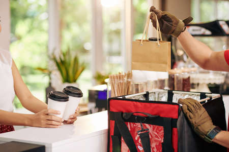 Cropped image of courier putting fresh non-dairy yogurt and cups of take away coffee in bag to deliver order from local cafeの写真素材
