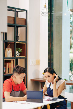 Small Vietnamese cafe owners working with financial documents and working on strategy of business...
