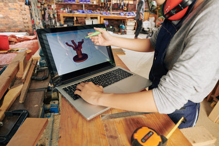 Female carpenter making 3D model of dinner table on laptop before making it