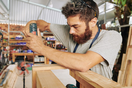 Serious carpenter assembling wooden stand in his studio, making furniture for customer