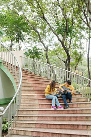 Parents and son sitting on steps, father playing guitar and others enjoying good musicの写真素材