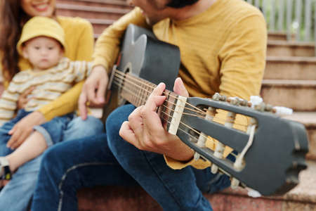 Close-up image of young man playing guitar for his cute little son, selective focusの写真素材