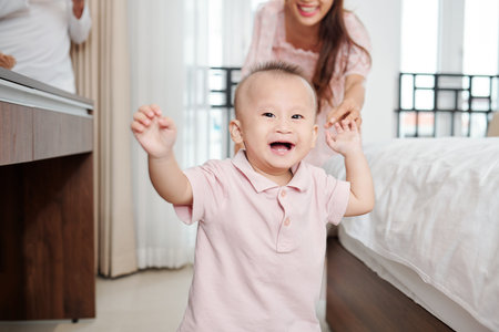 Happy young Asian woman releasing hand of her child who is smiling and walking to camera