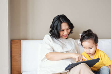 Smiling young mother showing educational application on tablet computer to her little daughterの写真素材