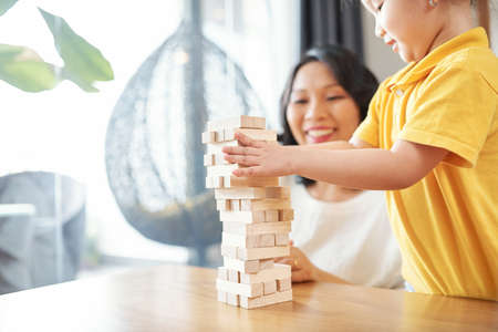 Little Asian girl and her mother playing with wooden bricks and making towerの写真素材