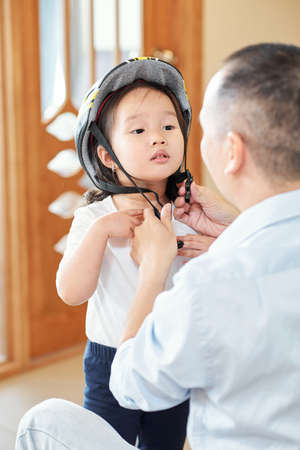Vietnamese man asking daughter to throw head back when he is fastening her bicycle helmetの写真素材