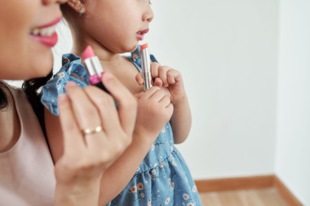 Close-up image of little girl applying light pink lipstick of her mother when they are getting ready for partyの写真素材