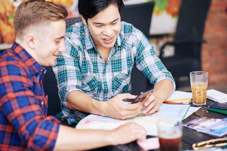Multi-ethnic young people having coffee in coffeeshop and discussing photos from summer vacation on...