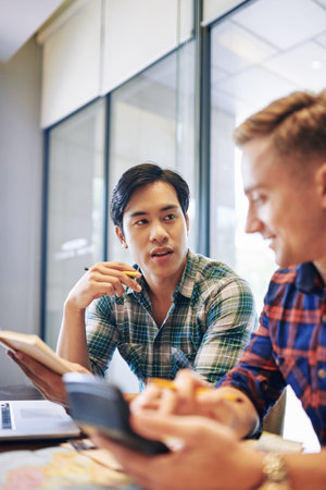 Handsome young Vietnamese man discussing project details with colleague at meeting