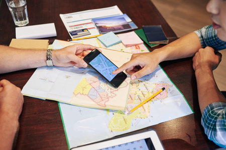 Young people planning trip, they are checking paper maps and online application on smartphone