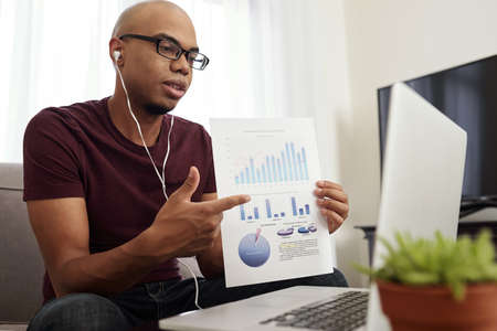 Young African-American financial analyst showing report to colleagues during online conferenceの写真素材