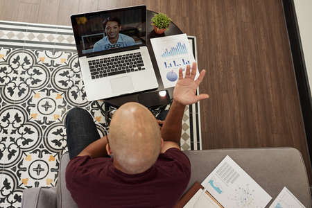 Young bald entrepreneur actively gesturing when having online meeting with colleague,view from aboveの写真素材