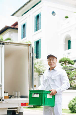 Smiling Vietnamese delivery man putting milk crates in van trunkの写真素材