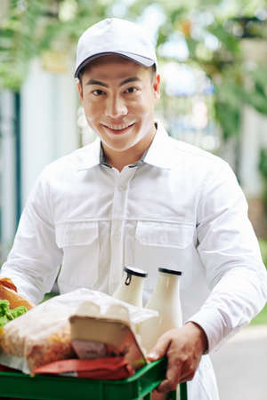 Smiling Vietnamese courier deliverying plastic crate of fresh products like milk, eggs and breadの写真素材