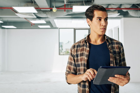 Young real estate manager visiting new building and filling information in database on tablet...