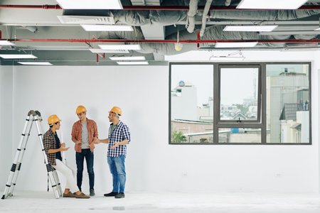 Young construction engineers in hard hats and plains shirts discussing news and gossips during short...