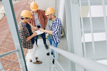 Young builders drinking morning cafe and checking plan of works on tablet computer