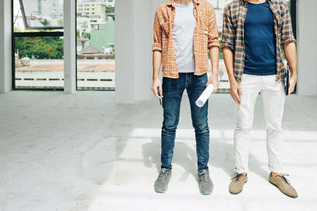 Cropped image of young engineers with blueprint and tablet computer standing inside building under constructionの写真素材