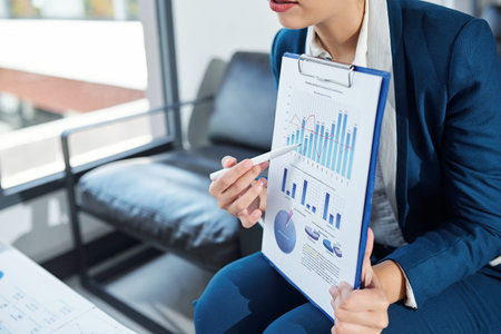 Cropped image of businesswoman pointing at bar chart in financial report when talking at meeting