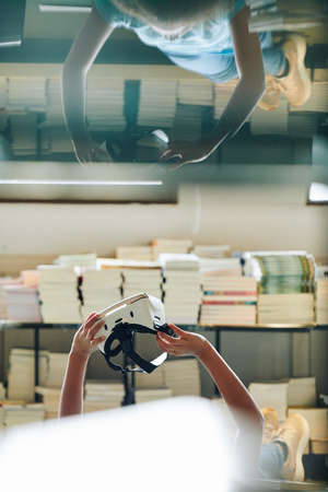 Teenage girl lying on library glasses with virtual reality headset in handsの写真素材