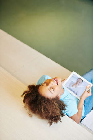 Teenage girl taking off earphones and laughing after funny joke of her teacher at online classの写真素材