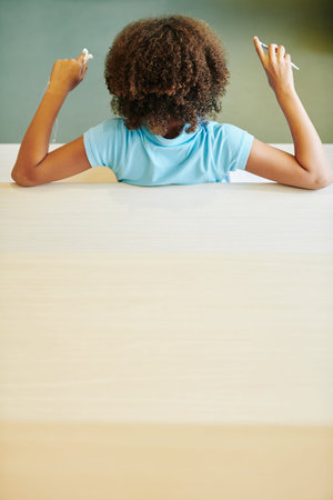 Mixed-race curly girl resting on sofa with pen and earbuds in hands, view from the back