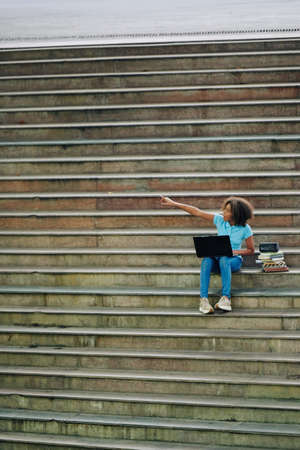 Excited teenage girl pointing away with her hand when sitting on steps with laptopの写真素材