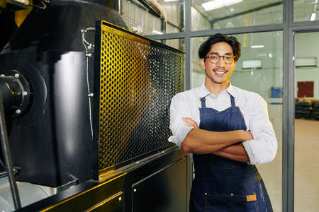 Portrait of cheerful confident smiling mixed-race man standing at coffee roaster and smiling at cameraの写真素材