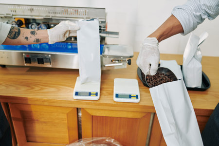 Hands of workers in rubber gloves weighting and packing coffee beans for selling