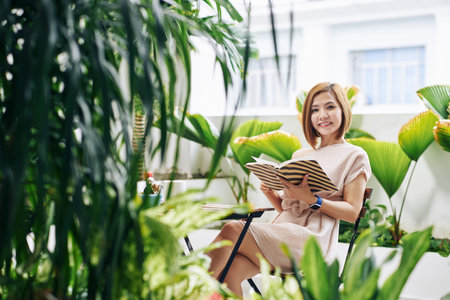 Portrait of attractive smiling young Asian woman enjoying reading book in cafe