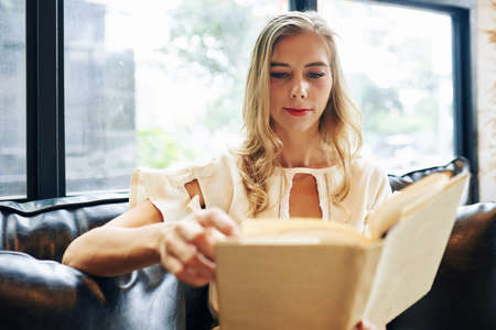 Young beautiful blond woman reading interesting novelの写真素材