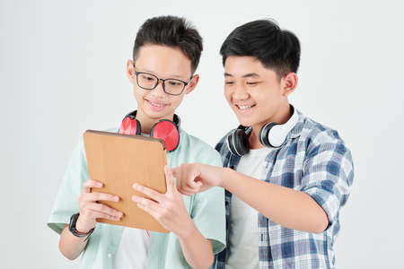 Excited Asian teenage boys discussing new application on tablet computerの写真素材