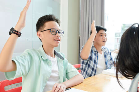 Smart students raising hands to show teacher that they know the answer to her questionの写真素材