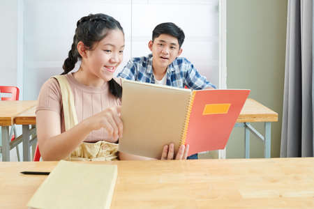 Smiling Vietnamese schoolgirl showing test answers in copybook to her friendの写真素材
