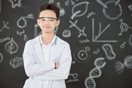 Portrait of happy little Vietnamese boy in labcoat and goggles crossing arms and looking at camera