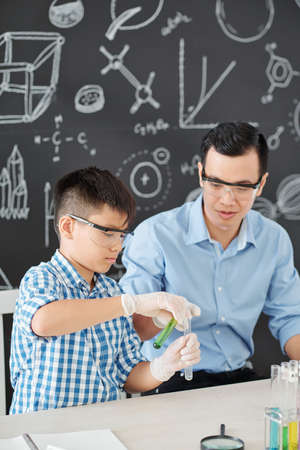 Vietnamese school student in goggles mixing reagents under control of chemistry teacherの写真素材