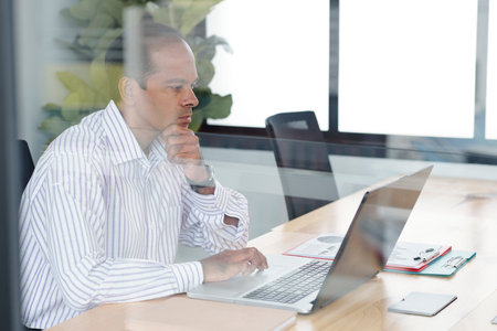 Serious concentrated mature Indian businessman reading document on laptop screen