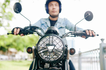 Serious Vietnamese man in helmet riding on motorcycle, focus on headlight