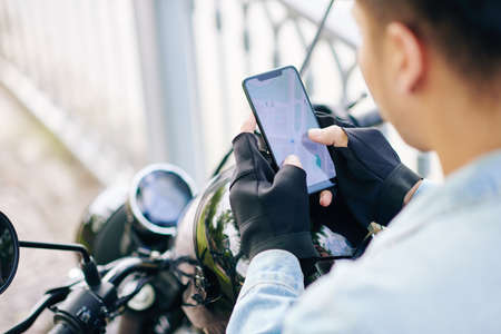 Motorcyclist in fingerless gloves checking map on smartphone screen before riding to destination pointの写真素材