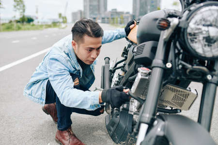 Serious concerned motorcyclist checking engine of motorcycle and searching for malfunctionの写真素材