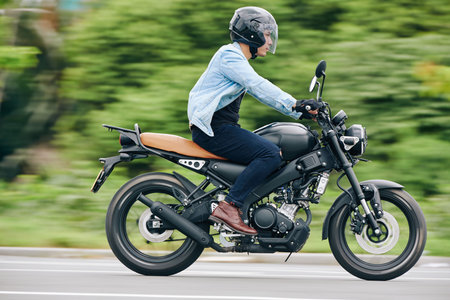 Serious Vietnamese man riding fast on motorcycle, blurred bushes in background