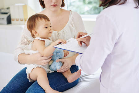 Curious little girl looking at medical history that pediatrician filling when talking to her motherの写真素材