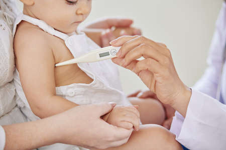 Close-up image of pediatrician checking temperature of little baby girl with electronic thermometerの写真素材