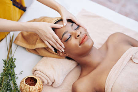 Smiling young woman getting relaxing rejuvenating face massage in spa salon, view from aboveの写真素材