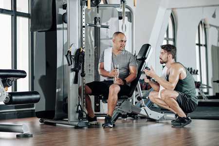 Professional fitness trainer and his client drinking vitamin water and talking during break