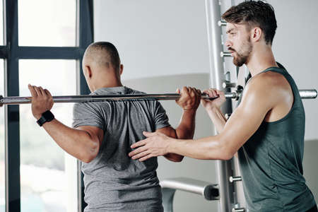 Serious fitness trainer controlling client getting ready to lift heavy barbellの写真素材
